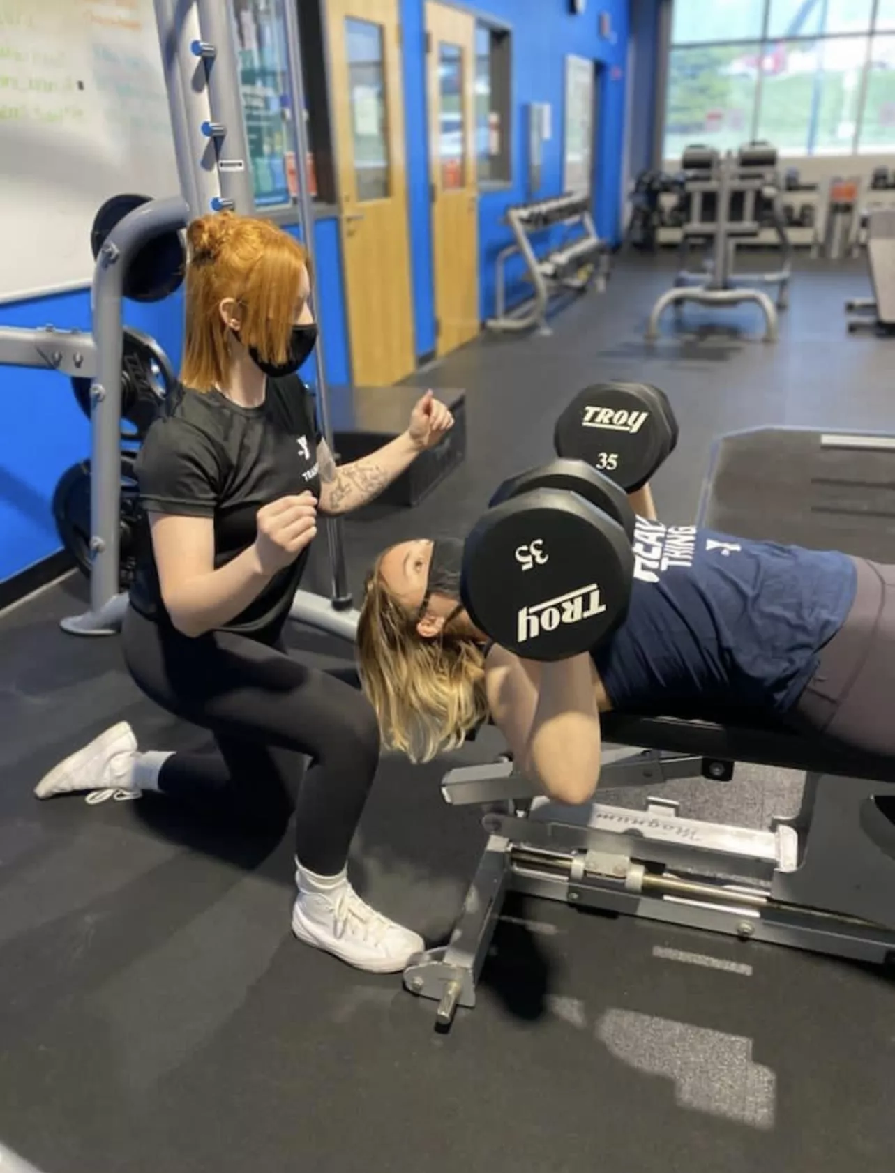 Teen girl lifting weights with a trainer