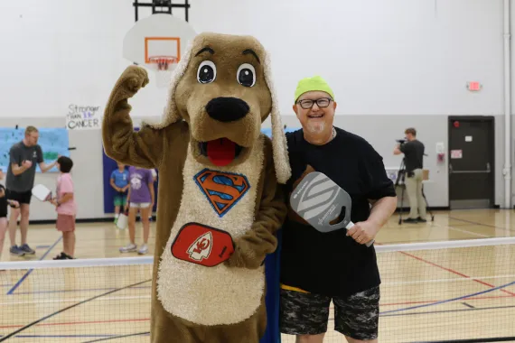 dog and man in gym holding pickleball paddles
