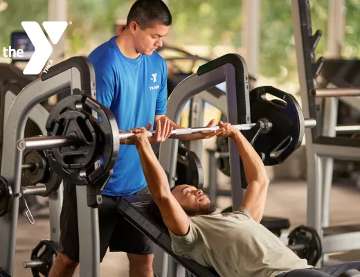 A personal trainer helping a young man with a lift