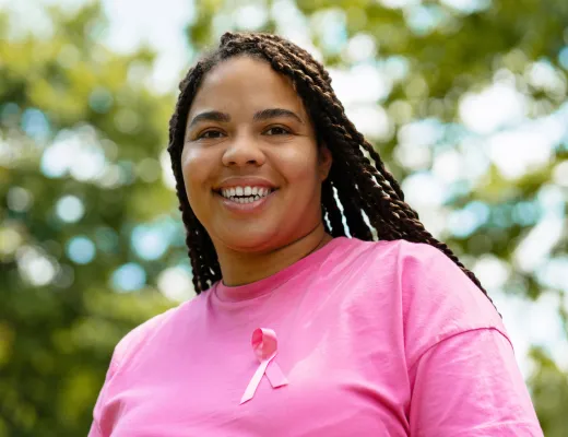 black woman in a pink shirt & ribbon smiling at the camera
