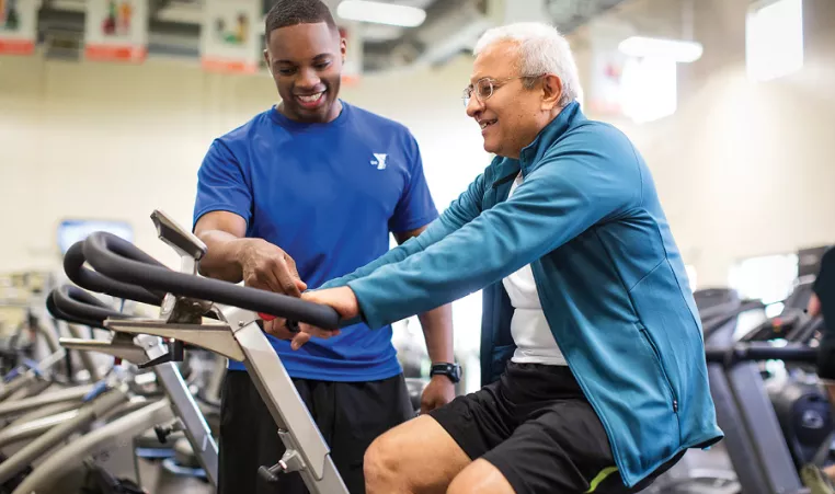 Gym employee helping senior man on stationary bike