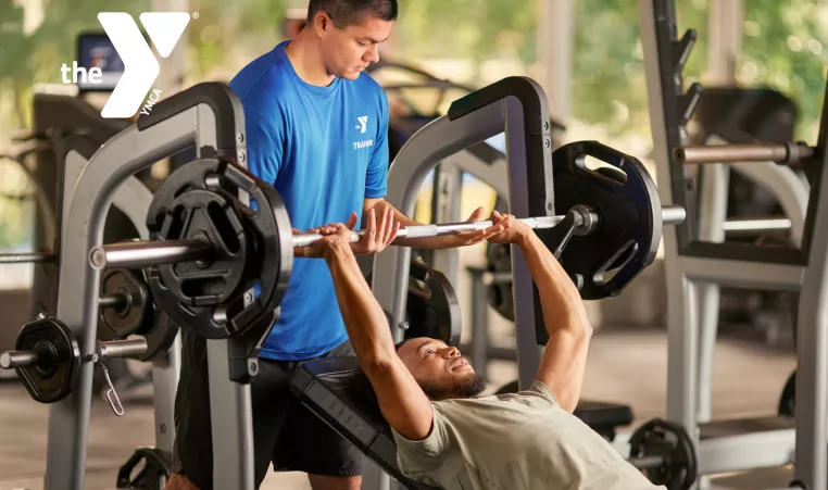 A personal trainer helping a young man with a lift