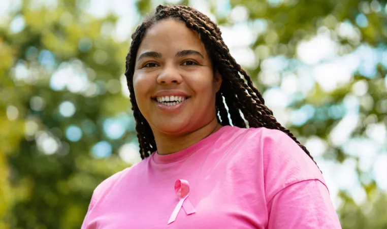 black woman in a pink shirt & ribbon smiling at the camera