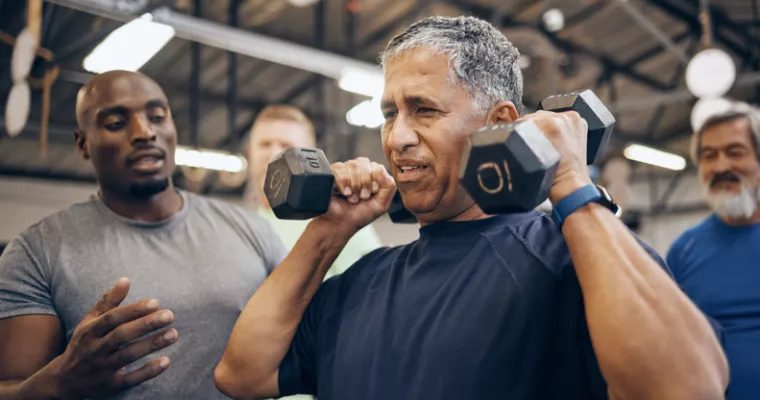 Older man lifting weights with a trainer